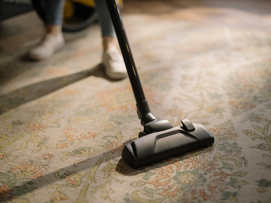 Three professional cleaners from Carpet Cleaners Acton are performing surface cleaning and deep cleaning in a modern living room with a light-colored tiled floor. The room features two large windows a